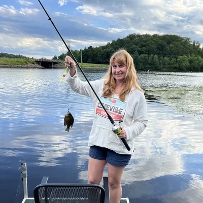 a woman with long light brown hair showing off a small fish she just caught