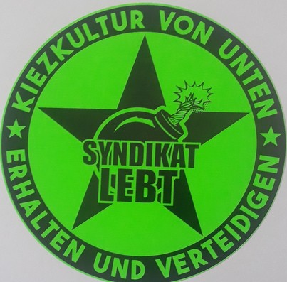 Neongrüner runder Aufkleber mit der Aufschrift: " Kiezkultur von unten  erhalten und verteidigen - Syndikat Lebt"