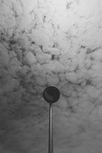 Es tut mir wirklich leid. Aber es ist für mich sehr schwierig dieses Bild zu beschreiben.

Zu sehen ist ein Strandduschkopf, von unten. Im Hintergrund ein Wolkenhimmel. Die Aufnahme wirkt aufgrund der kurzen Brennweite von 11mm sehr extrem.