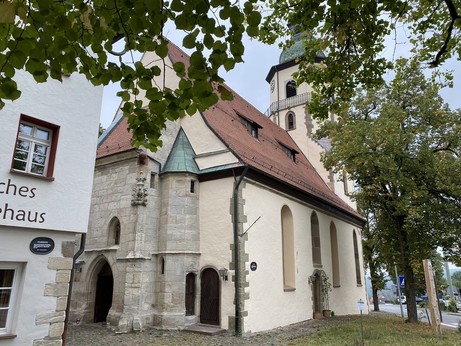 Einfache, alte einschiffige Kirche mit Chorturm. Turm unten viereckig, oben achteckig mit welscher Haube, Umgang und grün-glasierten Ziegeln. Im Westen kleine Vorhalle mit Treppenturm, gotischem Portal, zwei Fialen und Wasserspeiern. Im Vordergrund Lindenbäume und eingepflasterter Hof.