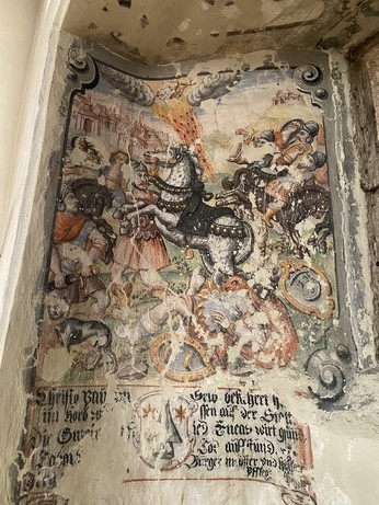Wandgemälde (Secco) in eine Nische, stark beschädigt. Gerahmt von einem aufgemalten Rahmen. Zentral ein sich aufbäumender Apfelschimmel und eine Feuerstrahl vom Himmel. Im Hintergrund Gebäude und Menschen in Rüstungen. Darunter eine fragmentarisch erhaltene Schrift.