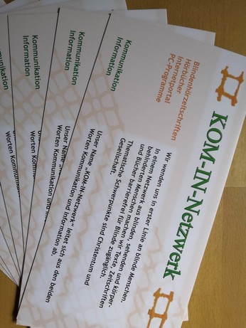 "Im Fächer ausgelegte Faltblätter: KOM-IN-Netzwerk, Textbeginn: Wir wenden uns an blinde Menschen...produzieren Hörzeitschriften"