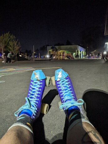 A pair of roller skates on a playground at night with people skating and a DJ in the background