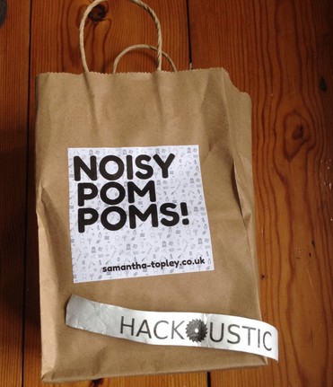 Photo of a Noisy Pom Poms! goodie bag with Sam Topley's website listed: samantha-topley.co.uk, alongside my Hackoustic event wristband.