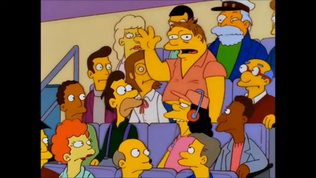 Barney Gumble (de la série "The Simpsons") se lève dans un public de télé en levant la main et en parlant.