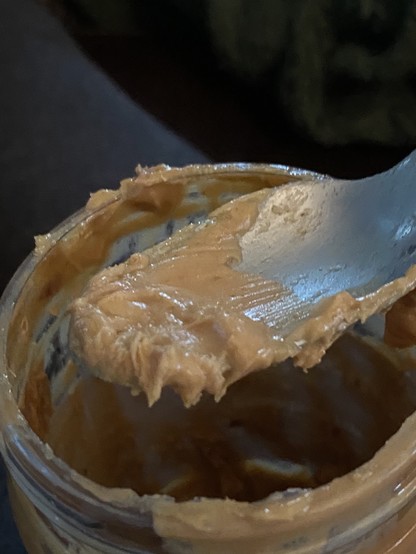 Half-eaten spoon of peanut butter hovering over an open jar.