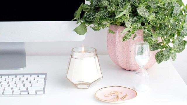 Calm desk workspace with iMac, keyboard, candle, a plant, and a sand timer.