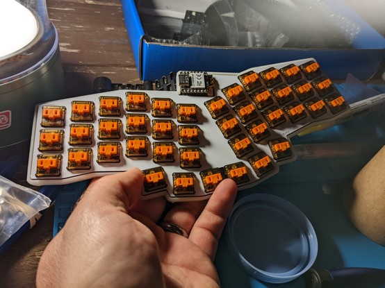 42 key unibody split low profile keyboard, without keycaps.

White switch plate, with orange "choc sunset" switches exposed. Small microcontroller visible in the center top of the keyboard.