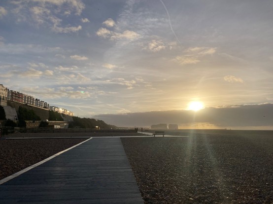Photo of the Brighton beach front looking east along the new board walk. The morning sun shines brightly over a bank of cloud and reflects off the buildings overlooking the sea from the terrace