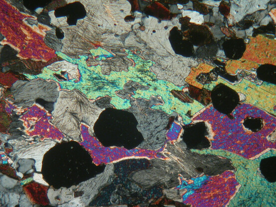 A 2mm wide crossed-polars microscope view of a rock from Knocknairling in the Scottish Southern Uplands. Black crystals of garnet, and brightly cooloured crystals of muscovite, with quartz, and little hair-like crystals of sillimanite.