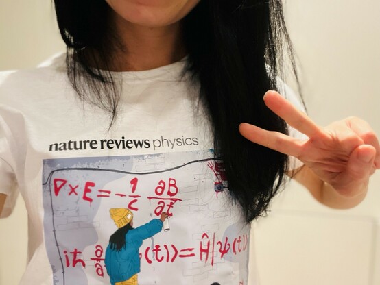 a picture of me in a t-shirt saying nature reviews physics with a cartoon of a young woman spray painting equations on a wall.