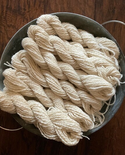 A round tin tray holding six mini skeins of undyed handspun wool yarn.
