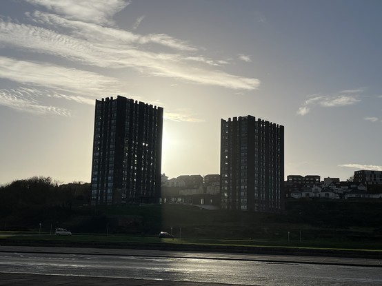 A photo of a double tower block silhouetted against the sun.