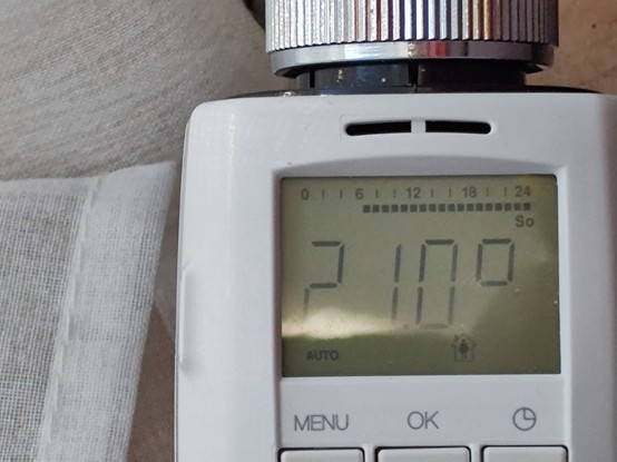 Picture of an installed electric programmable thermostat for radiator heaters showing a set temperature of 21°C
