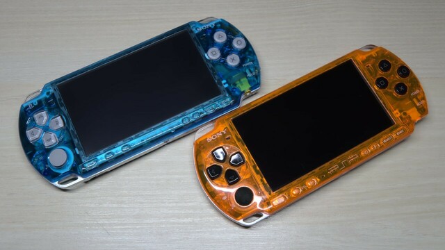 A PSP 2000 in a clear blue case with silver buttons, and a PSP 3000 in a clear orange case with black buttons.