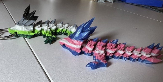 Two crystal dragons, colored in stripes representing the Trans Pride Flag (blue, pink, white, pink, blue) and the Aromantic Pride flag (bottom to top: dark green, light green, white, gray, black)
