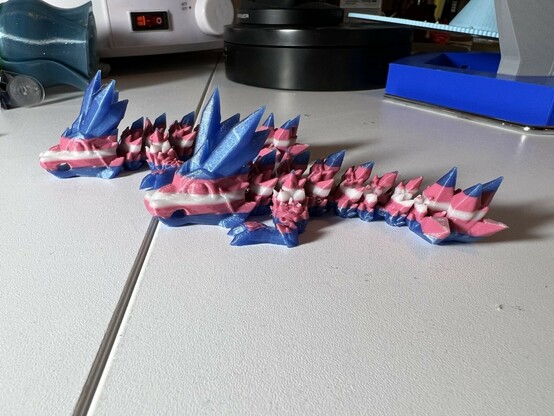 Two crystal dragons, both colored in stripes representing the Trans Pride Flag (blue, pink, white, pink, blue)
