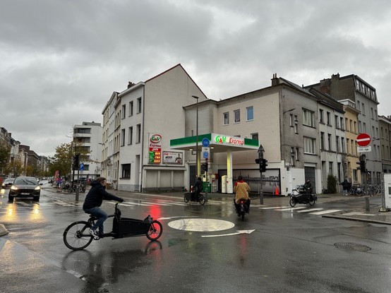 Photo of an urban petrol station on a rainy day, with some cyclist passing by.