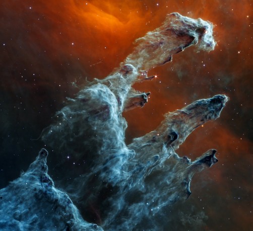 From NASA’s Flickr page: Three prominent pillars of semi-opaque gas and dust, each in spectral shades of gray-blue, start at the bottom left and reach toward the top right. From left to right, each pillar is consecutively smaller. Together, they appear like a ghostly hand. Towards the top of the leftmost pillar, there is one prominent red star, with tiny spikes at its tip. Lower on this pillar, there are several darker areas of dust that jut out like protrusions, some also with stars that appear as small red dots. The other two pillars are below and to the right of the first pillar. The background of this scene takes on glowing shades of orange-red mixed with black, with the strongest bright orange hues dipping into a V shape at the top center of the image. Scattered throughout the image are a few dozen tiny bright white and blue stars. Larger stars appear like red orbs and are embedded in the pillars.