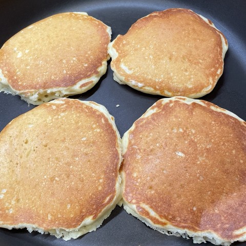 Four lightly browned buttermilk pancakes cooking in a nonstick skillet