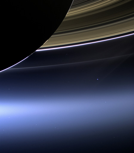 Earth appears as a small dot nestled beneath the rings of gas giant planet Saturn.