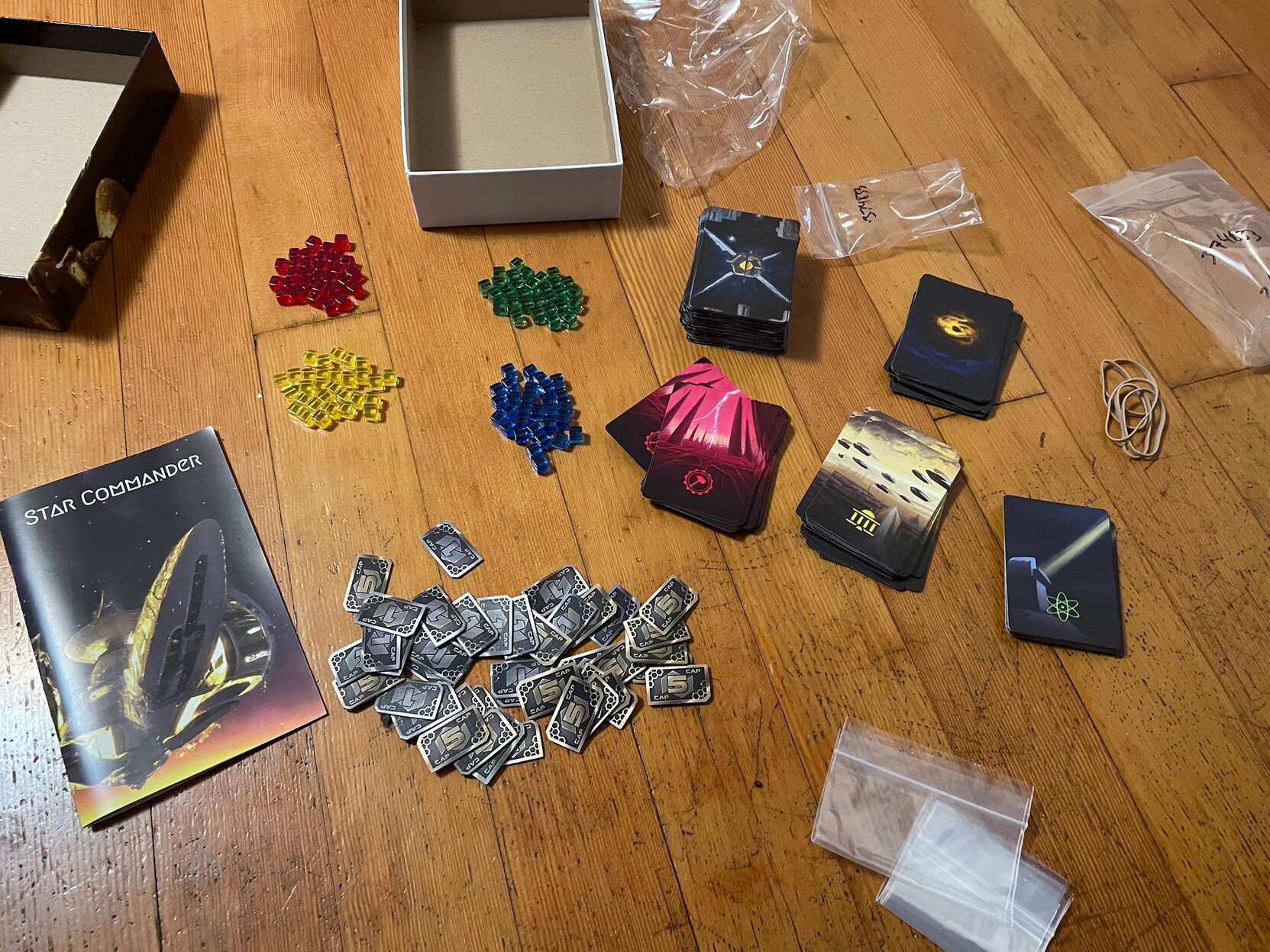 All of the components for Star Commander laid out on the floor, including plastic cubes, five decks, money tokens, and rulebook.