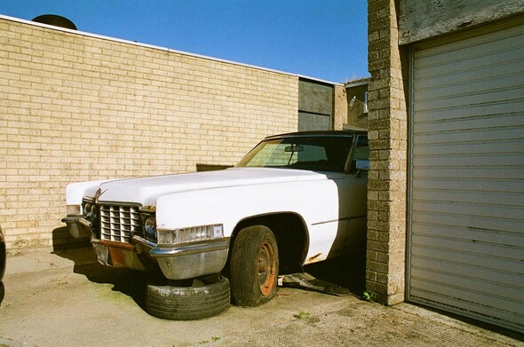 an old white american car with flat tyres parked between some brick garages