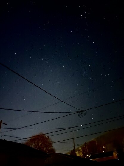 A dark sky full of stars with power lines crisscrossing the frame.