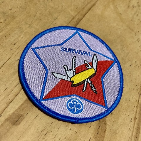 A girl guides fabric badge showing a Swiss Army knife and the word “Survival”