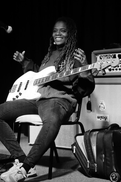 Black and white photo of bassist, vocalist, composer and producer Divinity Roxx smiling holding a Fender jazz bass 