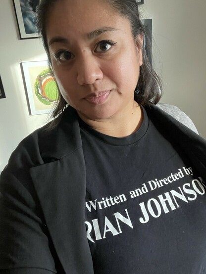 A woman wearing a black shirt with white text that says “written and directed by Rian Johnson”