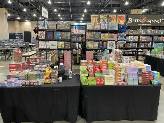 A counter in a convention hall destined in small games with some cool new titles displayed behind it. 