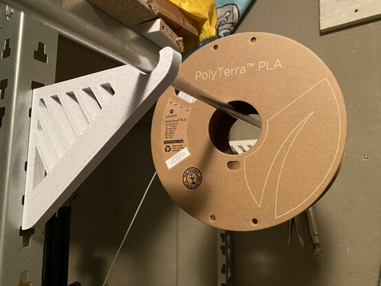 A spool of Polyterra PLa mounted on a 3d printed spool holder that is attached to slots on a shelving system.