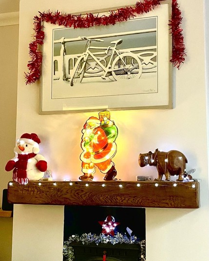 Living room mantelpiece with a fluffy snowman, lit up Santa and a hippo. Above is a picture of Hove seafront taken during a blizzard. An abandoned bike rests against the promenade railings all covered in a thick layer of snow. Photo my David Streeter