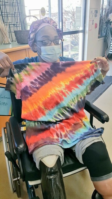 A wheelchair bound woman holding a multicolor striped tye dye shirt.