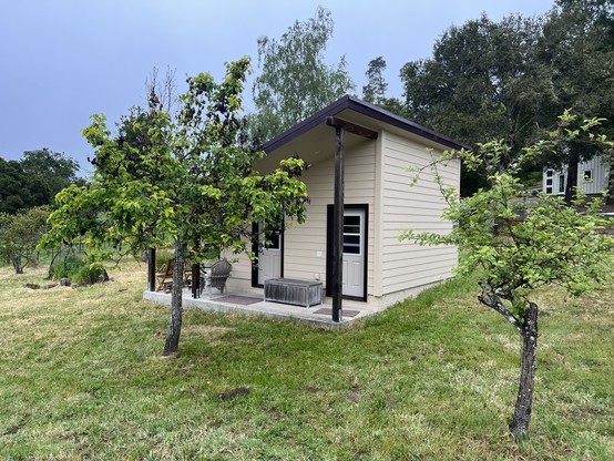 Rural scene with trees in foreground and background; in mid-ground is large shed with two doors and an angled roof pitched for solar panels