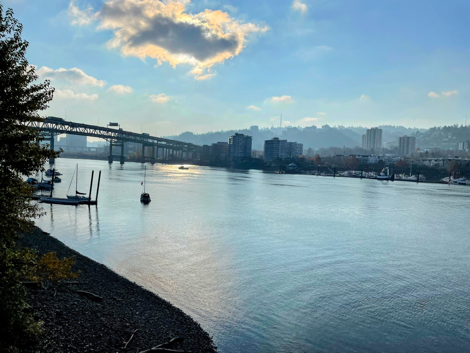Looking across the Willamette River towards downtown Portland, Oregon, with the sun reflecting gently on the river while hidden behind a cloud.