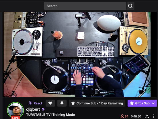 Screen shot of a browser with DJ Q*Bert skratchin on a live stream on https://twitch.tv/djqbert.

Visible is part of the so-called "Octagon" table from ThudRumble (https://www.thudrumble.com) which can host 4 mixers, 8 turntables and 4 deejays skratchin simultaneously!

On the left is a custom Technics SL-1200MK2 with a straight arm and a "flipped pitch" pitch shifter for "battle style" orientation with a Pioneer S9 mixer.

On the bottom of the picture is the setup DJ Q*Bert is skratchin on with this deejay set a Reloop (https://www.reloop.com/) ELITƎ mixer with two Reloop RP-8000MK2 turntables with straight arms customized by Jesse Dean Designs (https://jessedeancustoms.com/).