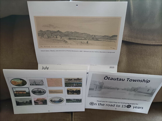 Photo of a calendar of Ōtautau Township for 2023. Top part of photo shows Thos. Blackwood's property "Kinloch" in a pencil drawing from 1883, at the bottom left the back page of the calendar has 12 small pics of each months images and on the bottom right, the front page of the calendar has a B & W Photo of the 1913 flood, with "On the road to 150 Years" and thank you for supporting our fundraising for this event.