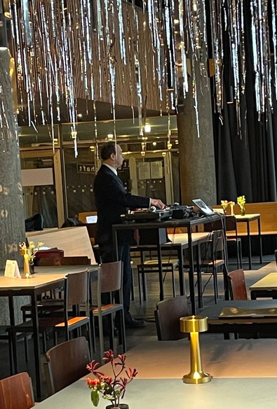 Restaurant, von der Decke hängt eine Art Lamettadeko, ein konservativ aussehender Mann in schwarzem Anzug legt Platten an einem freistehenden Hochtisch auf.
