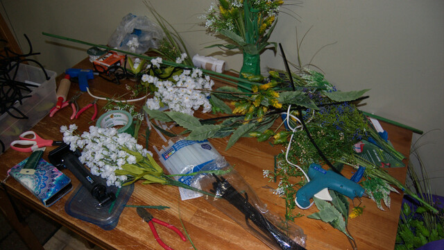 Table covered with crafting supplies (fake flowers, tools, glue guns, etc).