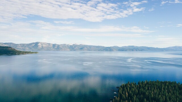 An aerial photo of Lake Tahoe, with softened reflections of the sky and clouds
