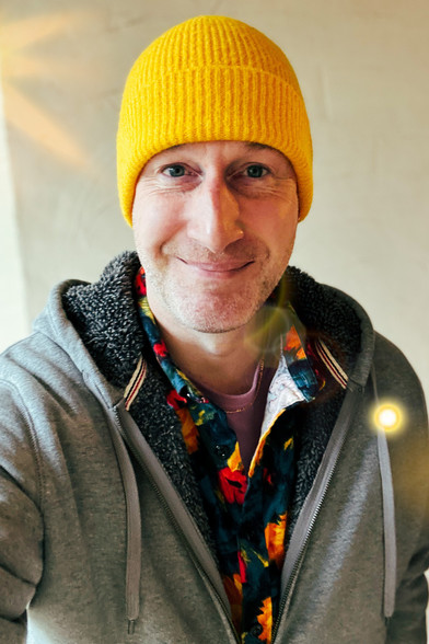 Sheepchase smiling in a yellow beanie and colorful shirt (and grey hoodie).