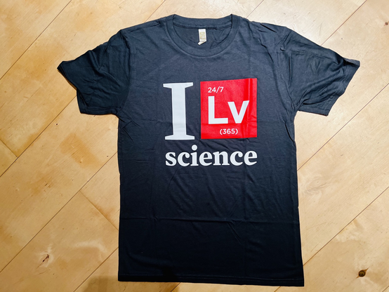 a black t shirt saying I Lv Science. the t shirt is laid on a wood panel floor.