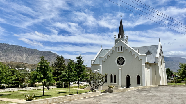 Old white church beside a green space with beautiful mountain and partly cloudy sky backdrop 