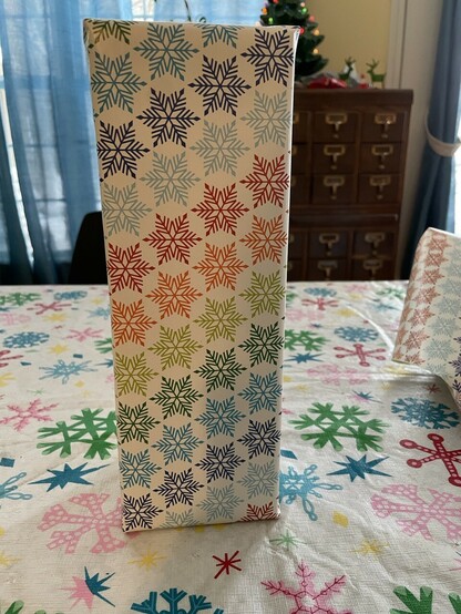 Present wrapped with paper that has rainbow colored snowflake on a white background. 