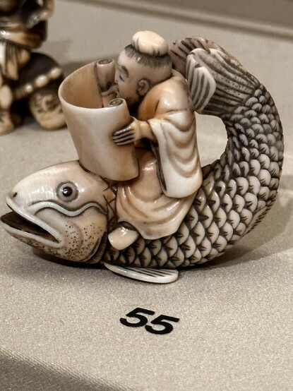An ivory Netsuke representing a monk reading a scroll riding a fish. 
