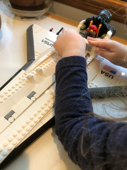 3yo hands adding LEGO to the wings engine block of the space shuttle. 