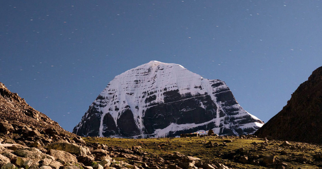 An image of Mt. Kailash in Tibet. The beautiful peak stands like a massive hulking entity again a grey-blue sky of stars. Many Buddhists consider Mt. Kailash to be the center of the earth. (Photo by Raimond Klavins. Image found in Tricycle magazine.)