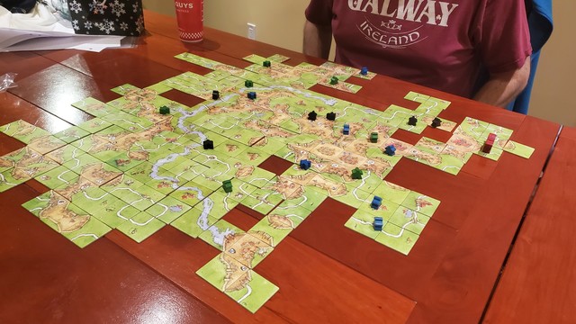 A large, four player Carcassonne layout on a wooden table.